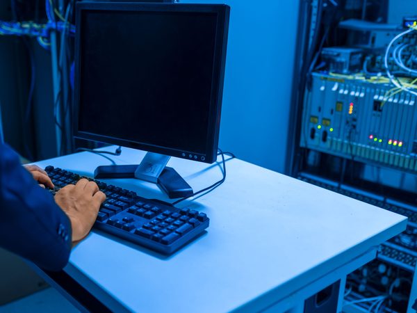 Technician typing at a keyboard in a blue-lit server room